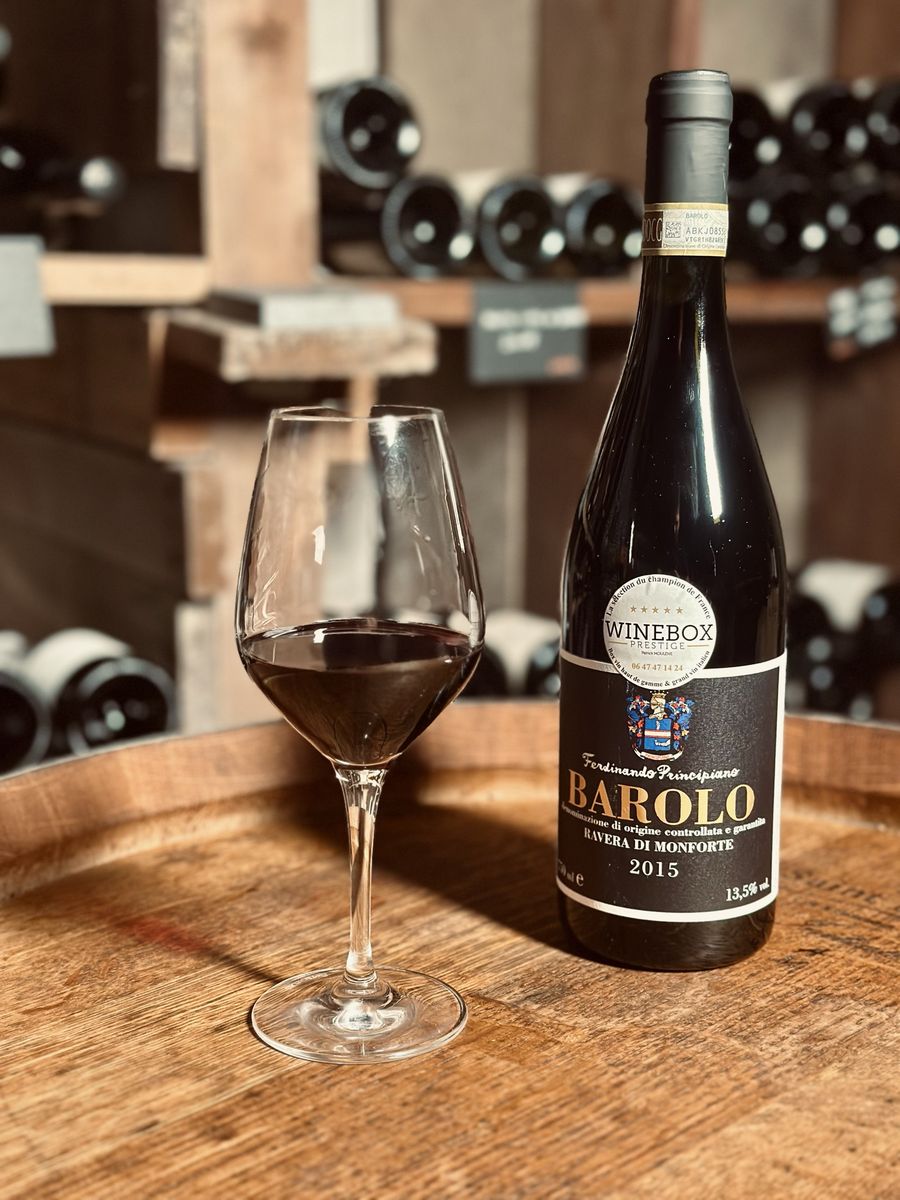 Un verre de Barolo et sa bouteille sur un tonneau, dans la cave